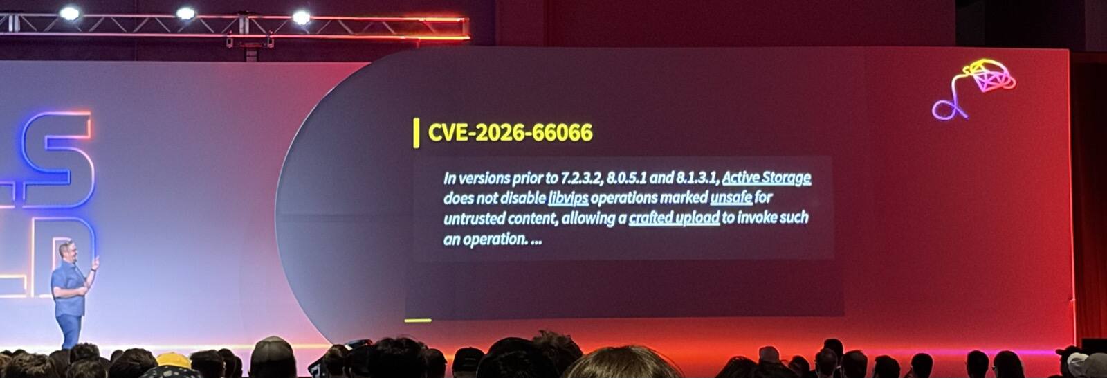 Mike Dalessio on stage at Rails World 2026 next to a slide titled 'CVE-2026-66066' that reads: 'In versions prior to 7.2.3.2, 8.0.5.1 and 8.1.3.1, Active Storage does not disable libvips operations marked unsafe for untrusted content, allowing a crafted upload to invoke such an operation.'