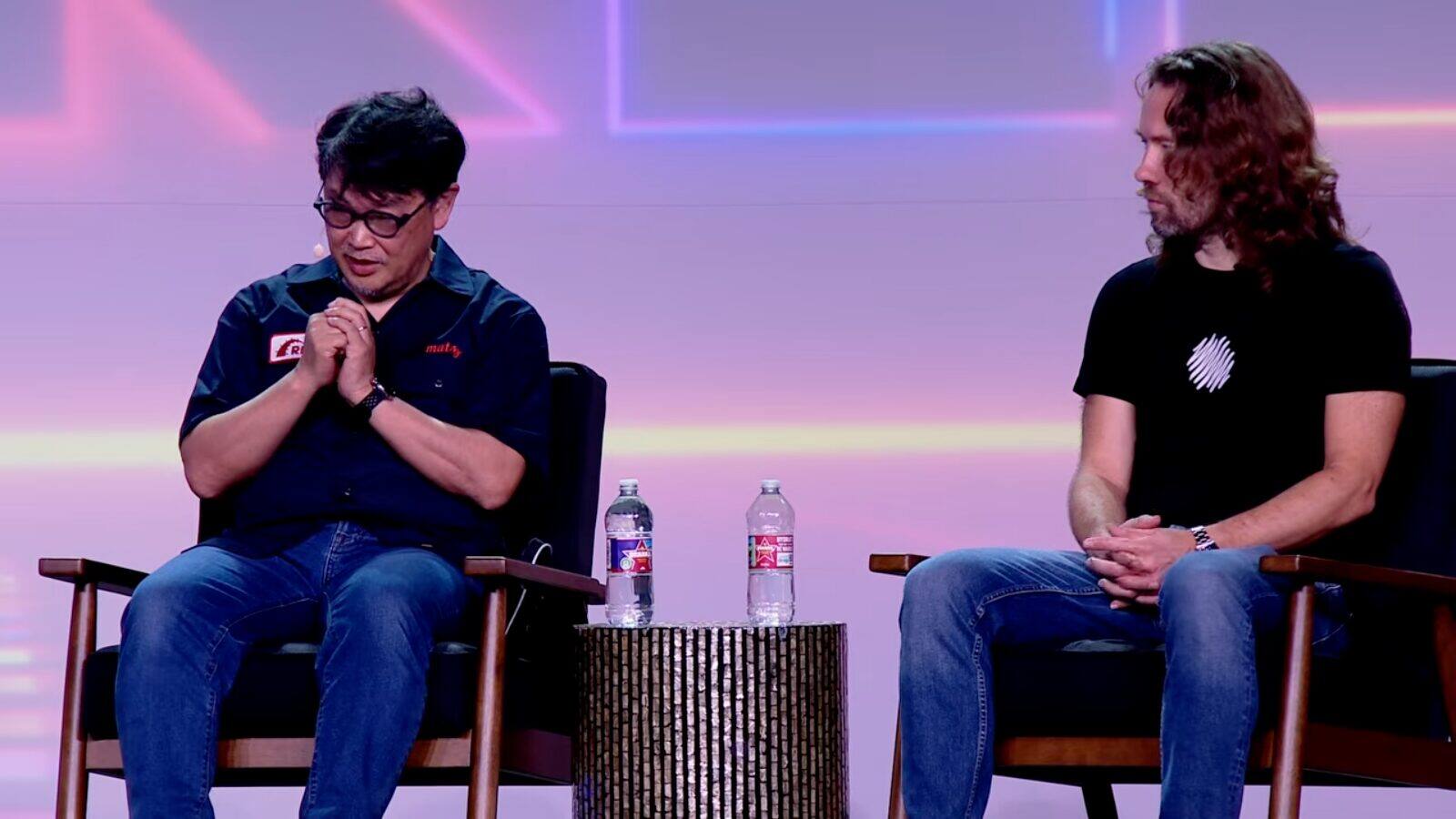 Matz and DHH sitting in armchairs on the Rails World 2026 stage, with water bottles on a small table between them